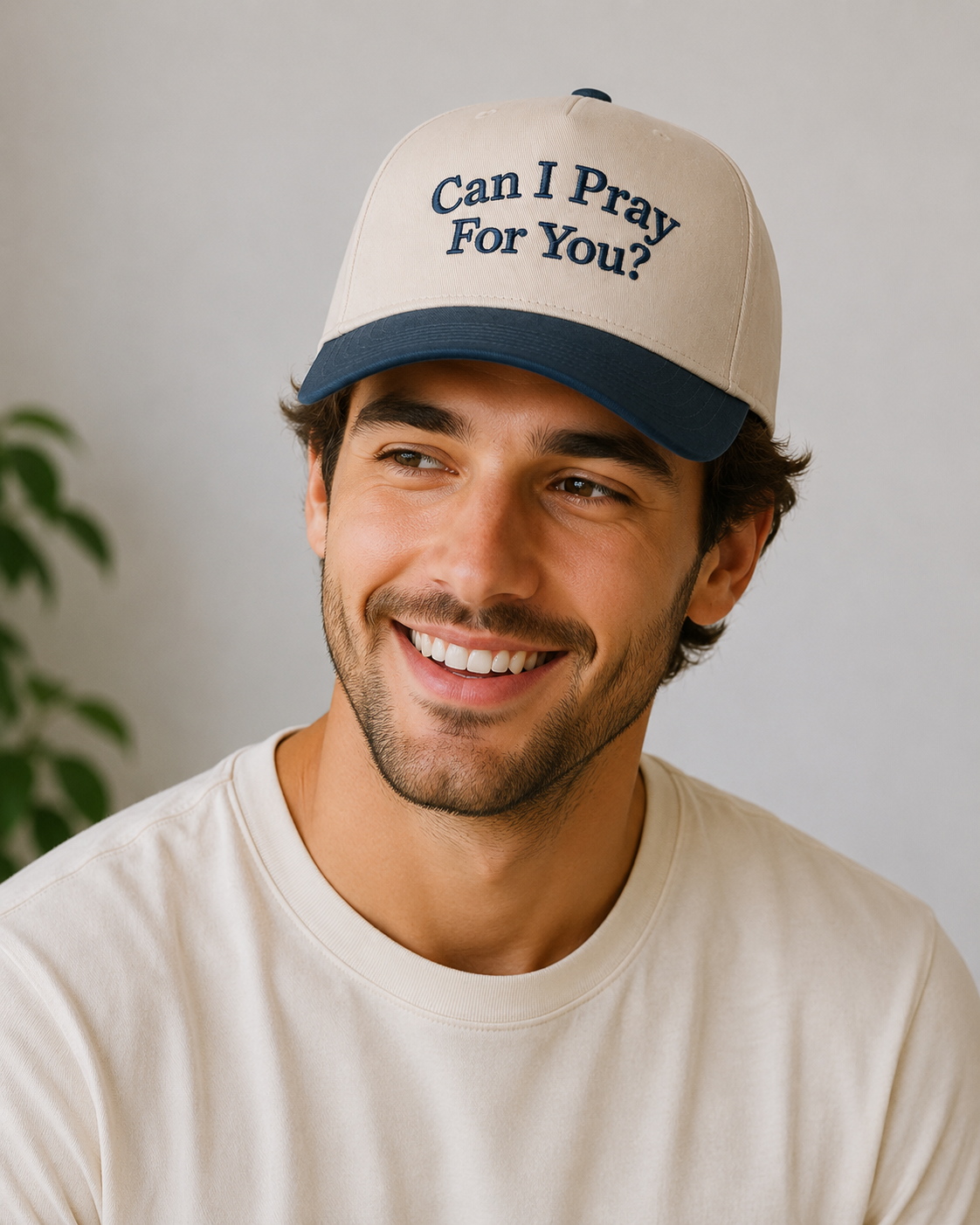 Man wearing a cap with 'Can I Pray For You?' text against a neutral background