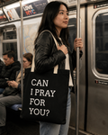 Woman holding a tote bag with 'Can I pray for you?' text on a subway train.